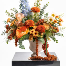 Large mixed floral arrangement in a beige vase with orange, blue, and cream blooms