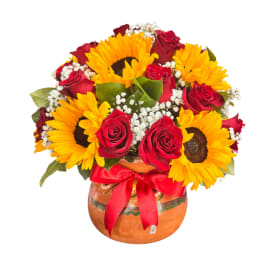 Sunflowers and red roses arranged in a round vase with a red ribbon