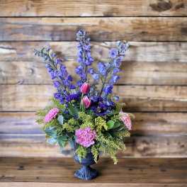 Purple and pink floral arrangement in a dark pedestal vase