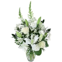 Tall white arrangement with lilies, roses, carnations, and snapdragons in a clear glass vase