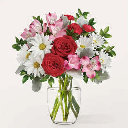 Bouquet of red roses, white daisies, and pink alstroemeria in a clear glass vase