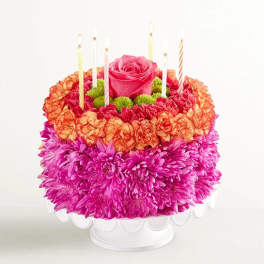 Round flower cake with a pink rose center and striped candles on a white stand