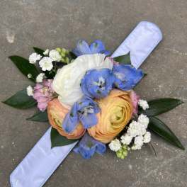 Hand-tied bouquet with blue, white, and peach flowers on a pale ribbon