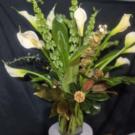 White calla lilies arranged in a clear glass vase with green accents