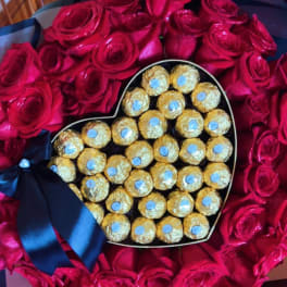 Heart-shaped box of chocolates surrounded by red roses with a blue ribbon