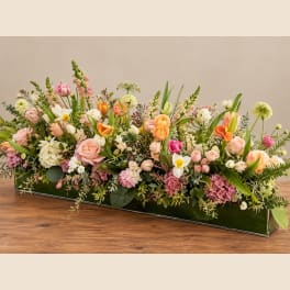 Low rectangular floral arrangement with pink, peach, white, and orange blooms