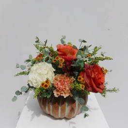 Orange and white floral arrangement in a pumpkin-shaped container