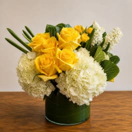 Yellow roses and white hydrangeas arranged in a green glass vase