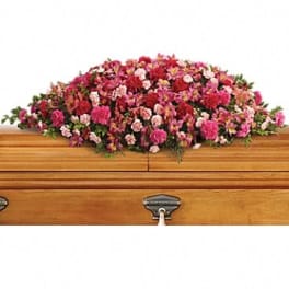 Pink and red floral casket spray on a wooden coffin
