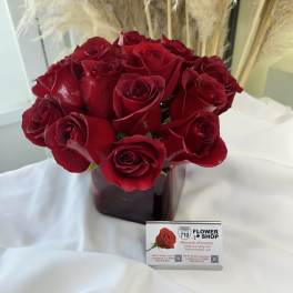 Red roses arranged in a dark vase with tall pampas grass behind them.