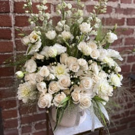 Large white and cream flower arrangement with roses and dahlias in a white ceramic vase