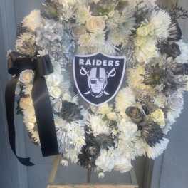 Heart-shaped white floral wreath with a Raiders emblem and black ribbon