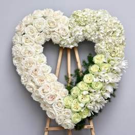 Heart-shaped floral wreath of white and pale green roses on a wooden easel