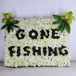White floral tribute with green orchids and leaves spelling "PAPA"