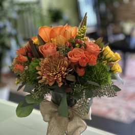 Orange and yellow bouquet in a glass vase with a burlap ribbon