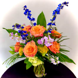 Orange roses and blue flowers in a glass vase