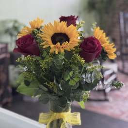 Bouquet of sunflowers and dark red roses in a glass vase