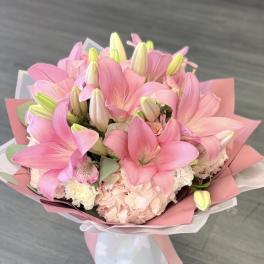 Pink lily bouquet in a white vase with pastel wrapping