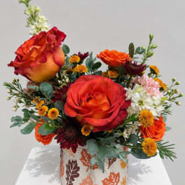 Orange and red roses arranged in a patterned vase with small accent flowers