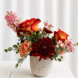 Mixed bouquet with orange-red roses and burgundy chrysanthemums in a patterned vase