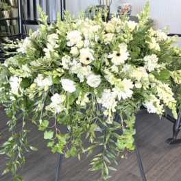 Large white floral arrangement with trailing greenery on a black stand