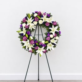 Purple and white floral wreath on a black easel stand