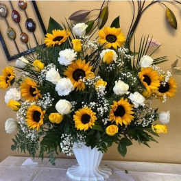 Large sunflower and white rose arrangement in a white pedestal vase