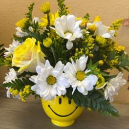Yellow and white daisy bouquet in a smiley-face vase
