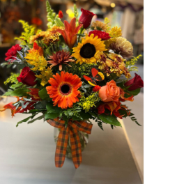 Autumn bouquet with sunflowers, roses, and orange blooms in a glass vase