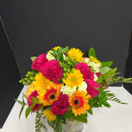 Mixed bouquet of pink roses and yellow-orange gerbera daisies in a glass vase
