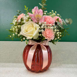 Pink and white flower arrangement in a red glass vase with a ribbon