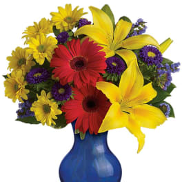 Colorful bouquet of yellow lilies, red gerberas, and purple daisies in a blue vase