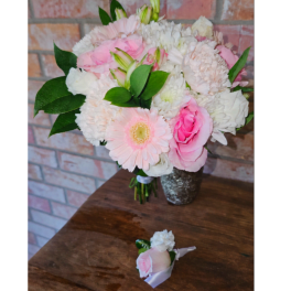 Pink and white bouquet in a silver vase with a matching boutonniere on a table