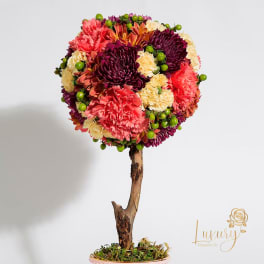 Round floral arrangement on a branch-like stem with pink, purple, and cream blooms