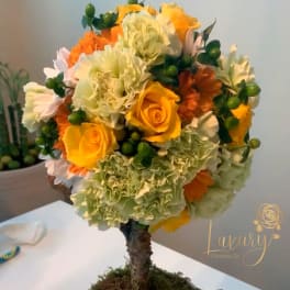 Round floral topiary in a white pot with yellow roses and orange blooms