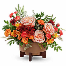 Arrangement of peach and orange roses with red flowers in a low container