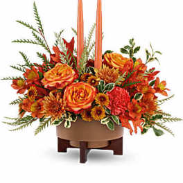 Orange floral centerpiece with two tall candles in a low bowl