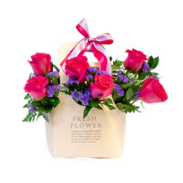 Pink roses in a cream gift bag with a ribbon bow