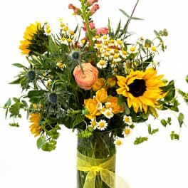 Mixed bouquet with sunflowers, daisies, and peach blooms in a glass vase