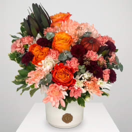 Mixed bouquet of orange roses, pink mums, and burgundy blooms in a white vase