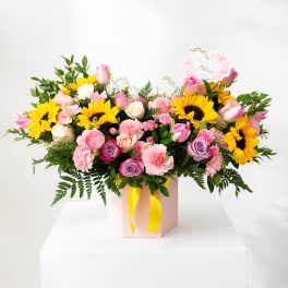 Mixed bouquet with sunflowers, roses, tulips, and carnations in a pink box