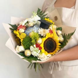 Bouquet of sunflowers, roses, and chocolates with a graduation cap topper
