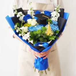 Bouquet of blue, white, and green flowers with a graduation cap topper