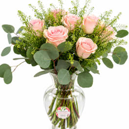 Pink roses arranged in a clear glass vase with eucalyptus foliage