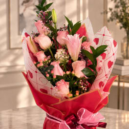 Pink roses and lilies in heart-patterned wrapping with a ribbon