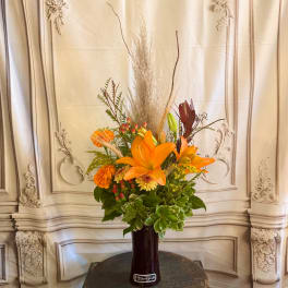 Orange lily arrangement in a tall dark vase with dried grasses