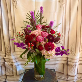 Tall mixed bouquet in a glass vase with pink, red, and purple flowers