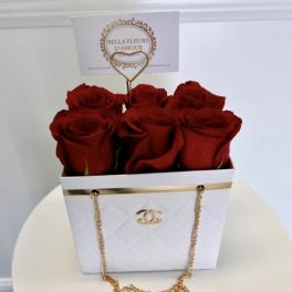Red roses arranged in a white gift box with a gold chain handle