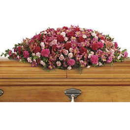 Pink and red floral casket spray on a wooden casket