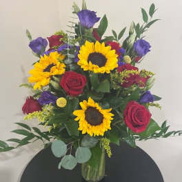 Bouquet of sunflowers, red roses, and purple blooms in a glass vase